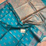 Vibrant sea green pure Bhagalpuri Munga silk saree from Bhavya Lakshmi Fabrics featuring small multi-color floral butis and an intricate gold zari border with pink accents, spread on a wooden floor.