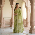 Sophisticated olive green linen blend Bhagalpuri saree featuring white geometric Bagru prints and elegant pompom tassels.