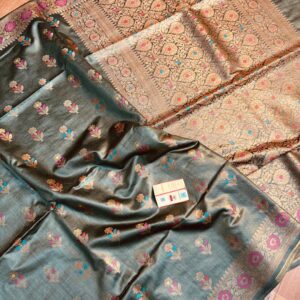 Sophisticated steel grey pure Bhagalpuri Munga silk saree from Bhavya Lakshmi Fabrics featuring multi-color floral butis and an intricate gold zari border, spread on a wooden floor.