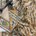 An unstitched cream Katan silk suit material set by Bhavya Lakshmi Fabrics featuring detailed multi-colored Madhubani prints of royal elephants, peacocks, and human figures in teal blue and mustard yellow.
