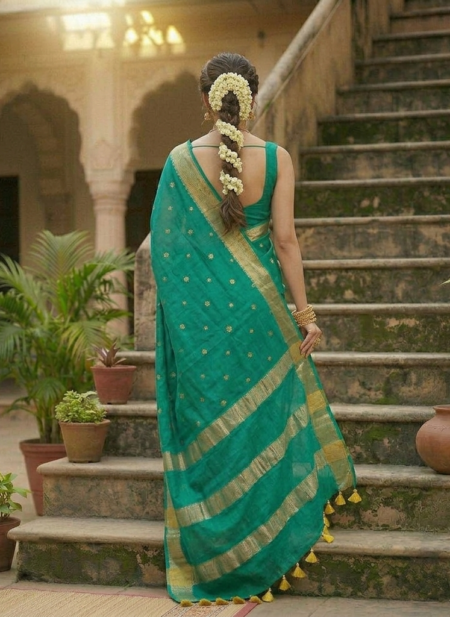 A woman poses in a teal green Kota silk Bhagalpuri saree featuring gold floral buta embroidery and a wide gold zari border on a set of stone steps.