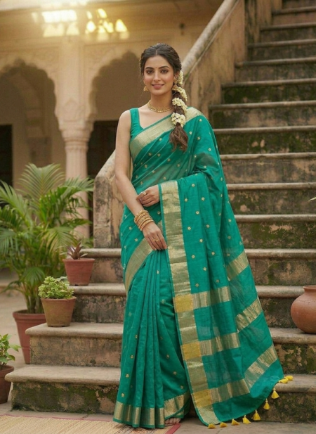 A woman poses in a teal green Kota silk Bhagalpuri saree featuring gold floral buta embroidery and a wide gold zari border on a set of stone steps.