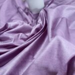 A close-up view of premium, handloom lavender Tassar Munga pure silk fabric by Bhavya Lakshmi Fabrics draped under a white potted tulip flower ornament.