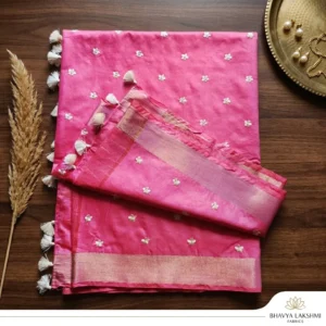 A woman wearing a vibrant pink Kota Silk Bhagalpuri saree with a wide gold zari border and white tassels standing on stone steps.