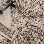 An unstitched beige Katan silk suit material set by Bhavya Lakshmi Fabrics featuring detailed black and magenta Warli tribal dance prints, geometric borders, and a matching dupatta.