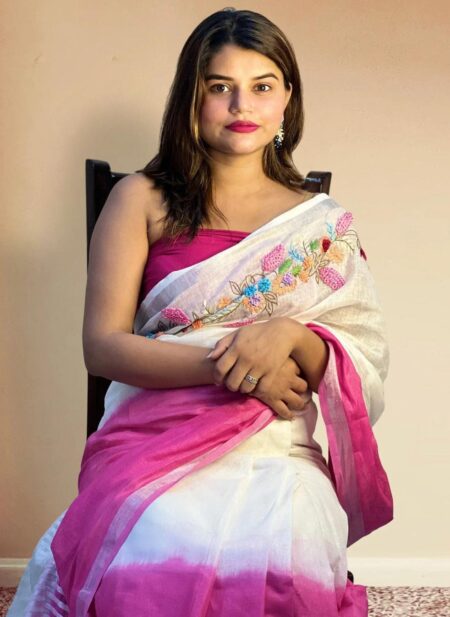 An Indian model showcases a white pure linen saree by Bhavya Lakshmi Fabrics featuring colorful floral embroidery across the shoulder and a vibrant magenta pink border.