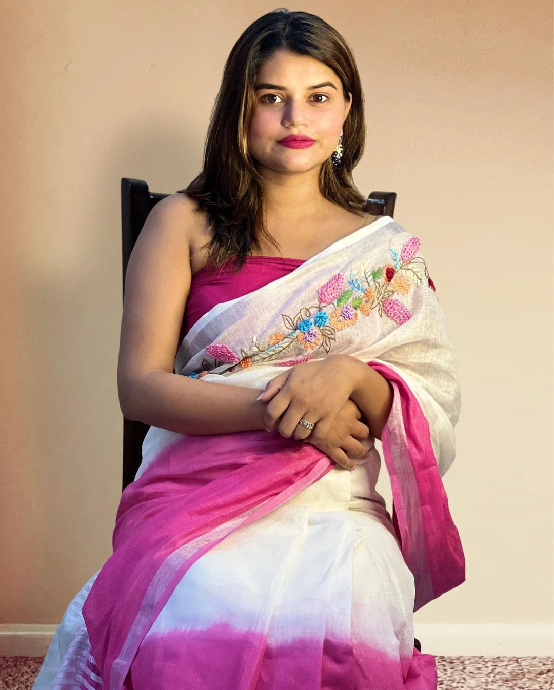 White and Pink Embroidered Bhagalpuri Pure Linen Saree An Indian model showcases a white pure linen saree by Bhavya Lakshmi Fabrics featuring colorful floral embroidery across the shoulder and a vibrant magenta pink border.