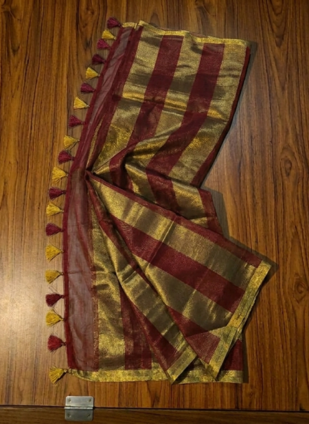 Rich maroon and metallic gold zari striped tissue silk saree featuring intricate borders and matching tassel details.