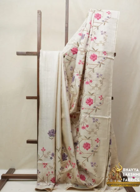 Bhavyaloom natural cream 100 percent pure tussar muga silk saree with pink and purple floral hand embroidery draped on wooden stand