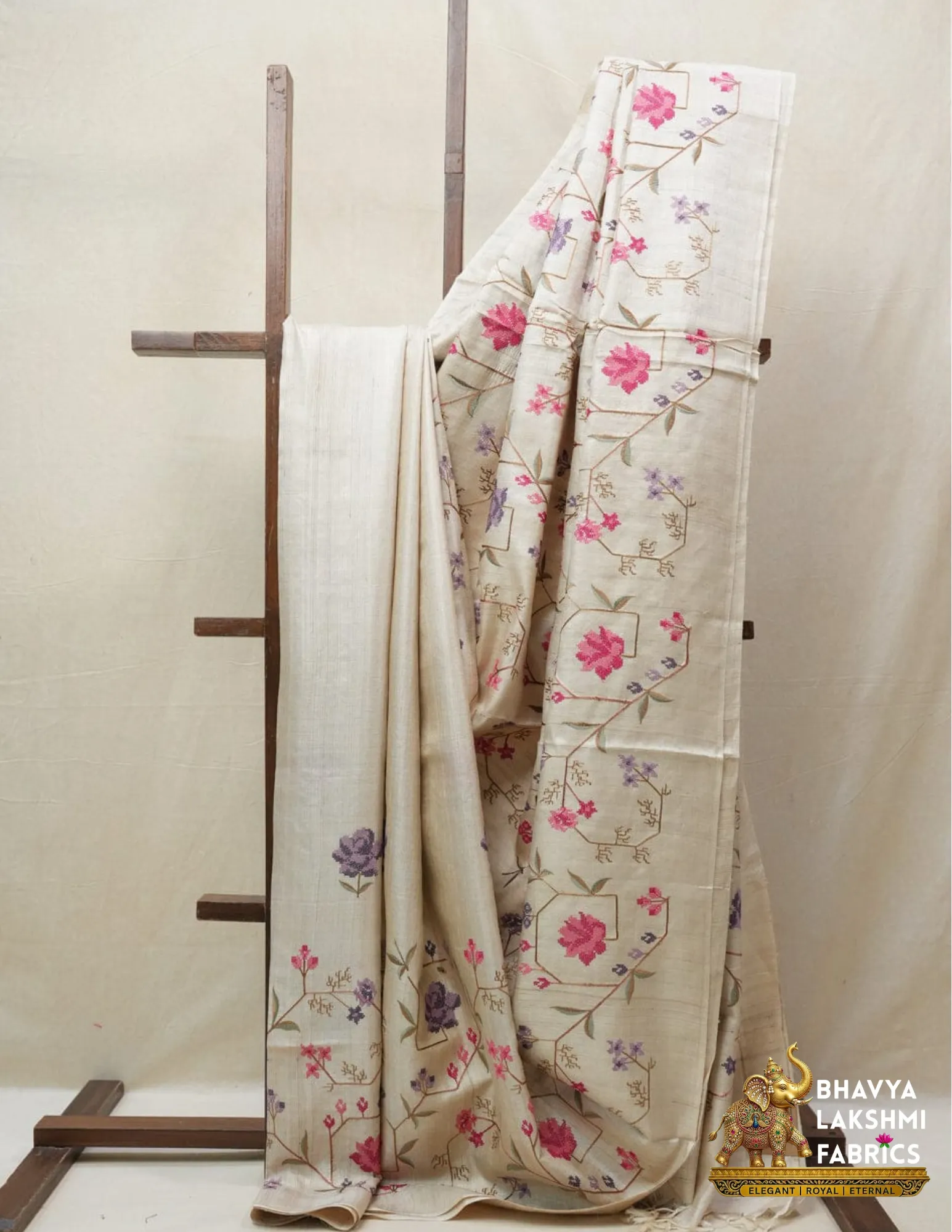 Handwoven 100% Pure Tussar Munga Silk Saree – Natural Cream by bhavyaloom_result Bhavyaloom natural cream 100 percent pure tussar muga silk saree with pink and purple floral hand embroidery draped on wooden stand