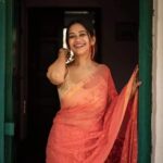 Bhavyaloom peach pink bhagalpuri kota doria embroidery saree with gold border on smiling model standing in doorway