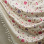 Bhavyaloom natural cream 100 percent pure tussar muga silk saree with pink and purple floral hand embroidery draped on wooden stand