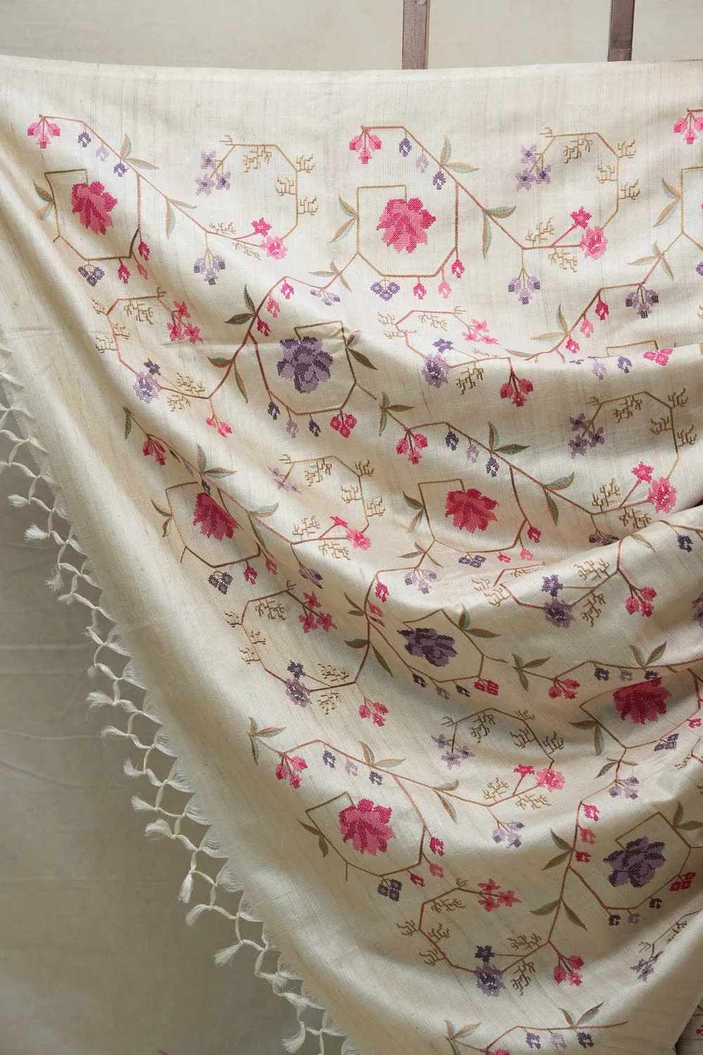 Handwoven 100% Pure Tussar Munga Silk Saree – Natural Cream 1_result Bhavyaloom natural cream 100 percent pure tussar muga silk saree with pink and purple floral hand embroidery draped on wooden stand