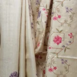 Bhavyaloom natural cream 100 percent pure tussar muga silk saree with pink and purple floral hand embroidery draped on wooden stand