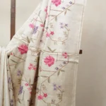 Bhavyaloom natural cream 100 percent pure tussar muga silk saree with pink and purple floral hand embroidery draped on wooden stand