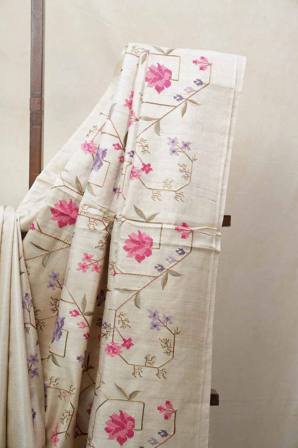 Handwoven 100% Pure Tussar Munga Silk Saree – Natural Cream by bhavyaloom_result Bhavyaloom natural cream 100 percent pure tussar muga silk saree with pink and purple floral hand embroidery draped on wooden stand