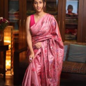 A model poses elegantly in a luxurious rose pink pure Tussar Munga Bhagalpuri silk saree. The saree features a rich, luminous texture decorated with all-over hand-embroidered floral jaal patterns in magenta, violet, and deep purple threads. The palla is beautifully finished with matching knotted thread tassels