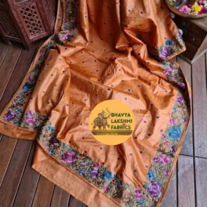 A luxurious rust orange pure Tussar Munga silk saree laid flat, featuring scattered small dark embroidered dots across the body and an intricate border adorned with vibrant multicolored floral embroidery in shades of purple, violet, blue, and green leaves. The textile displays a rich, textured wild silk grain