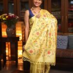 A model poses elegantly in a luxurious sunshine yellow pure Tussar Munga Bhagalpuri silk saree. The saree is adorned with intricate all-over floral jaal embroidery featuring pink, violet, and orange blossoms on delicate green vines. The palla features neat hand-knotted tassels.