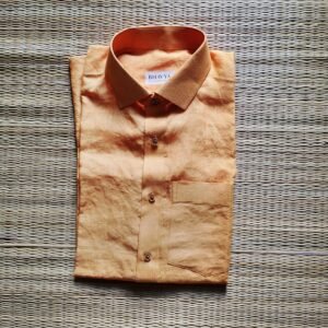 A luxurious peach orange pure handloom linen shirt laid flat on a woven straw mat background. The shirt features a clean button-down collar, a neat front chest pocket, and a white brand label reading Bhavya Loom