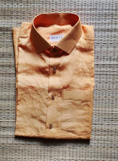 A luxurious peach orange pure handloom linen shirt laid flat on a woven straw mat background. The shirt features a clean button-down collar, a neat front chest pocket, and a white brand label reading Bhavya Loom